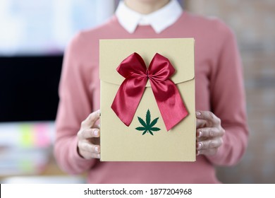 Female hands hold box with bow and marijuana logo. Marijuana delivery concept