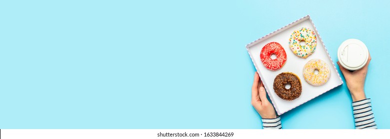 Female hands hold a box with donuts, a cup of coffee on a blue background. Concept confectionery store, pastries, coffee shop. Banner. Flat lay, top view - Powered by Shutterstock