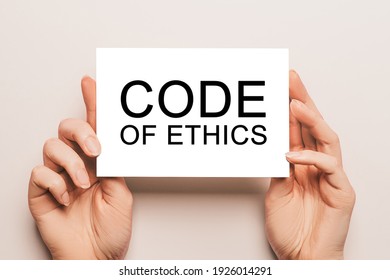 Female Hands Hold Card Paper With Text Code Of Ethics On A Yellow Background. Business And Finance Concept