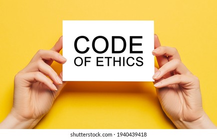 Female Hands Hold Card Paper With Text Code Of Ethics On A Yellow Background. Business And Finance Concept