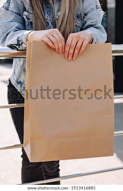 Female hands hold a cardboard bag in the\
street. Delivery received. Place for a\
logo.