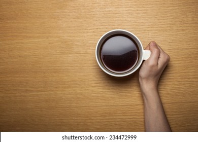 A Female Hands Hold A Cup Of Coffee On The Wood Table(desk), Top View At The Studio.