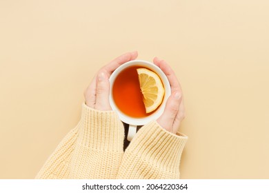 Female hands hold cup of tea with lemon. Hands with sweater hold cup of tea top view on beige background, winter and autumn concept - Powered by Shutterstock