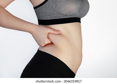 female hands hold a fold of skin on the side, the concept of excess weight, visceral fat, sagging skin after pregnancy and childbirth, healthy lifestyle, beautiful figure