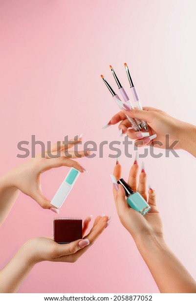 Female hands hold nail\
polish, brushes and other manicure products on a pink background.\
Catalog photo