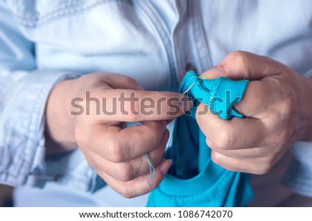 Female hands hold a needle with a thread and some clothes to mend it