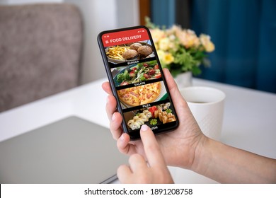 Female Hands Hold Phone With Food Delivery Application On Screen Against Background Of Room In House