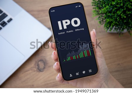 female hands hold phone with IPO stocks purchase app on screen at table in office 