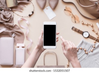 Female Hands Hold Phone On Fashion Apparel Background, Girl Customer Shopper Using Online Mobile Shopping App Choosing Buying Stylish Trendy Cloth With Mobile Payments On Cell Tech, Close Up Top View