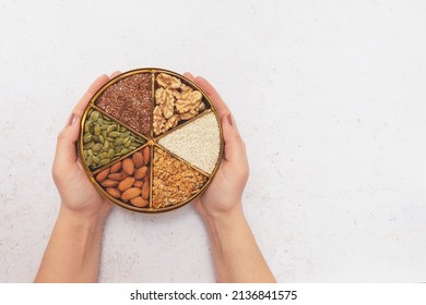 Female hands hold a plate divided into sectors with various seeds and nuts. Concept: vegetarian and vegan food. Natural nutrition