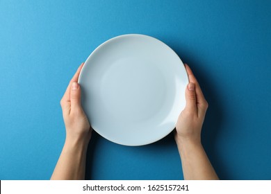 Female hands hold plate on blue background, top view