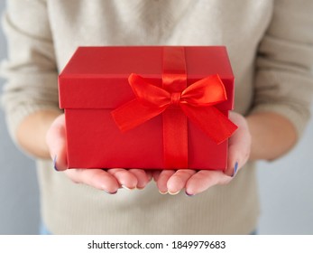 Weibliche Hände halten eine rote Geschenkbox. Geburtstag und Weihnachtsgeschenk mit roter Schleife und Band. Gib ein Geschenk in einer Schachtel. Zeit für Geschenke und Weihnachten.