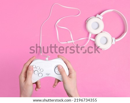 Female hands hold retro gempads on pink background with headphones. Gaming concept
