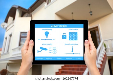 Female hands hold a tablet computer with system clever house on a screen on the background of the house