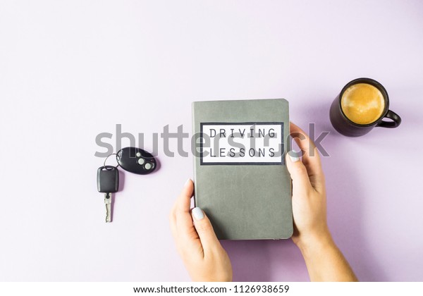 Female hands hold a training book for driving\
lessons and studying traffic rules. Getting a driving license\
concept. On a violet\
background