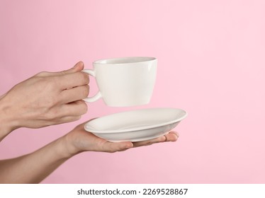 Female hands hold a white ceramic cup with a saucer on a pink background