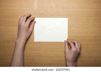 A female hands hold(grip) a white envelope on the wooden desk, top view at the studio. - Shutterstock ID 233737591