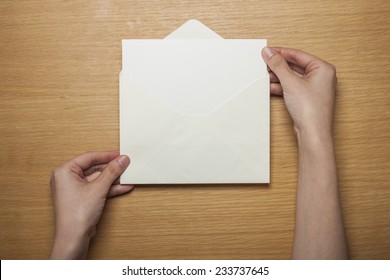 A Female Hands Hold(grip) A White Envelope And Postcard On The Wooden Desk, Top View At The Studio.