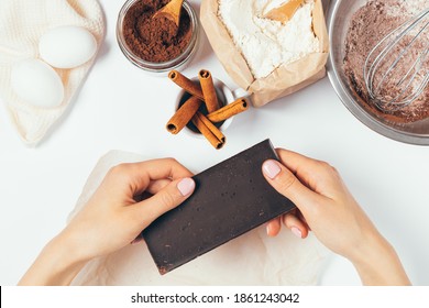 Female hands holding bar of dark chocolate next to ingredients for baking homemade brownie with cinnamon on white table, top view. - Powered by Shutterstock