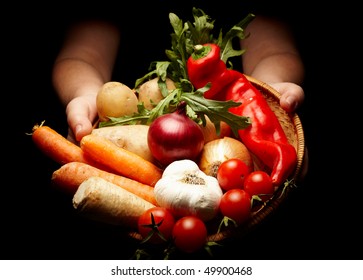 female hands holding a basket full of vegetables isolated on black