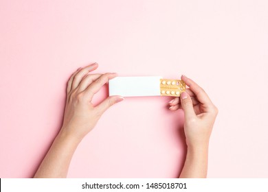 Female hands holding birth control pills on pink background. Women contraceptive hormonal birth control pills. Planning pregnancy concept.