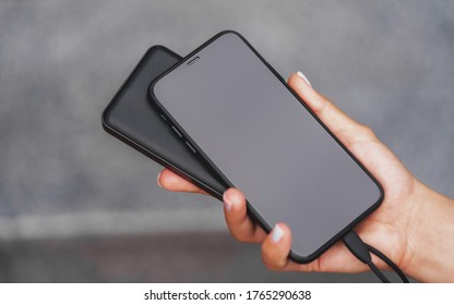 Female Hands Are Holding A Black Phone And A Black Powerbank Charger. Still Life Modern Digital Concept.