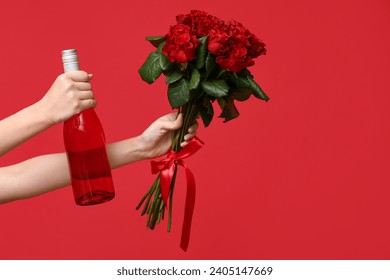 Female hands holding bottle of wine and roses on red background. Valentine's Day celebration