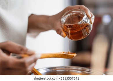 Female hands holding a bowl of bee honey and a wooden spoon. Close up. Elaboration of organic soap based on glycerin.
