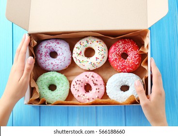Female hands holding box with colorful donuts on blue wooden background