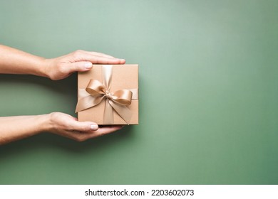 Female hands holding Christmas gift box on pastel green background.