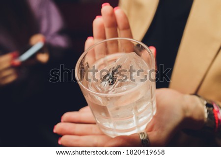 Female hands holding a clear glass of water. Slime body on background.
