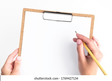 female hands holding a clipboard with a white sheet of paper on a white background. woman about to write a note on empty blank with a pencil, top view