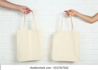 Female hands holding cotton eco bags on white brick wall background - Powered by Shutterstock