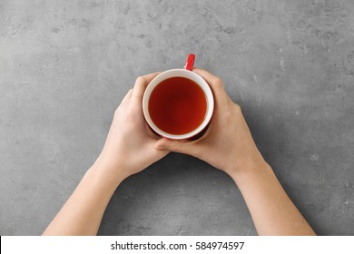 Female Hands Holding Cup Of Aromatic Tea On Grey Background