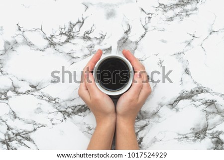Female hands holding cup of black coffee on white marble background. Flat lay top view. Morning breakfast concept.