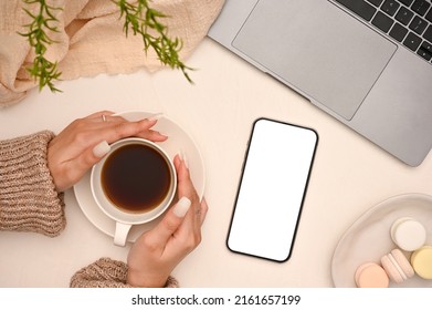 A Female Hands Holding A Cup Of Coffee In Her Minimal Beautiful Workspace Office Desk With Laptop, Smartphone Mockup And Decor On White Background. Top View