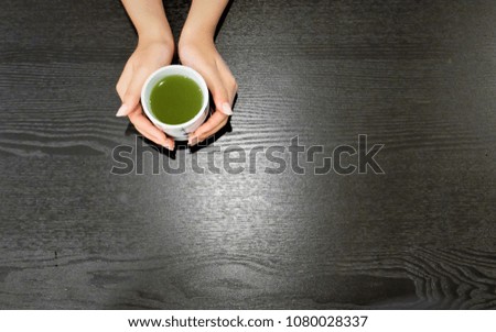 Female hands holding cup of green matcha tea on black background