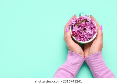 Female hands holding cup with lilac flowers on turquoise background - Powered by Shutterstock