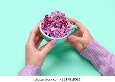 Female hands holding cup with lilac flowers on turquoise background - Powered by Shutterstock