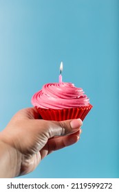 Female Hands Holding Cupcake With With Birthday Candle Close Up, On Blue Background.