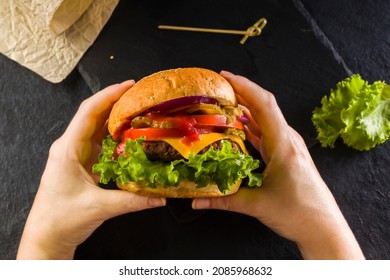 Female hands holding a delicious juicy burger. View from above. Fast food. Lifestyle