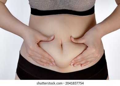 female hands holding a fold of skin on the abdomen, the concept of excess weight, visceral fat, saggy skin after pregnancy and childbirth,