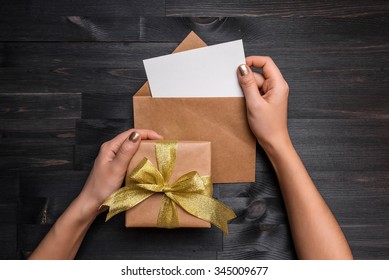 Female Hands Holding Gift Card And Gift Box Over The Black Wooden Table