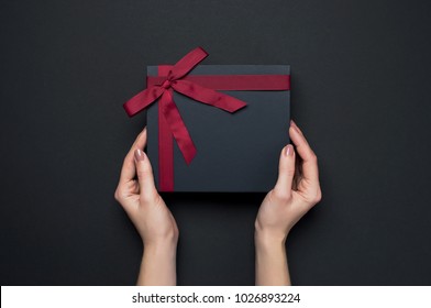 Female hands holding a gift with a red ribbon, one object on a dark background. Gift holiday. Festive background. Top View Flat Lay Advent Gift - Powered by Shutterstock