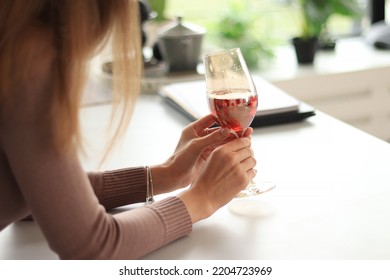 Female hands holding a glass of red wine, close up shot with selective focus. Drink in hands against the backdrop of a bright kitchen - Shutterstock ID 2204723969