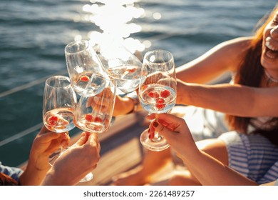 Female hands holding glasses of champagne with raspberries on board the boat. Sunset sky and sea on the background. Making a celebratory toast with sparkling wine. Birthday, holiday, party and friends - Powered by Shutterstock