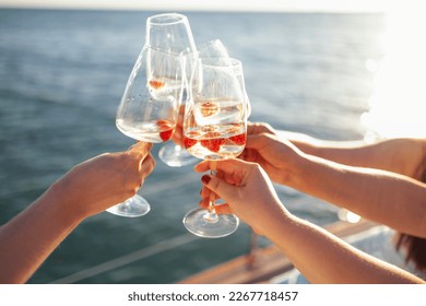 Female hands holding glasses of champagne with raspberries on board the boat. Sunset sky and sea on the background. Making a celebratory toast with sparkling wine. Birthday, holiday, party and friends - Powered by Shutterstock