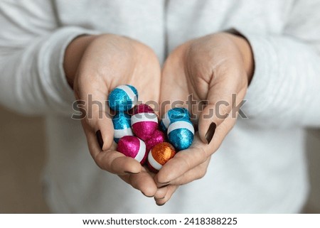 Female hands holding a group of mini Chocolate Easter Eggs wrapped in multicoloured foil