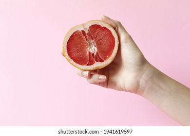 Female hands holding half grapefruit on pink background, female masturbation concept. High quality photo