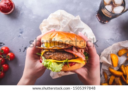 Female hands holding juicy beef burger. American fastfood.  Top view